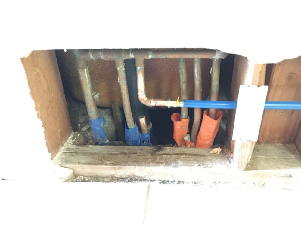 Pipes with color-coded connectors showing plumbing installation behind a wall.