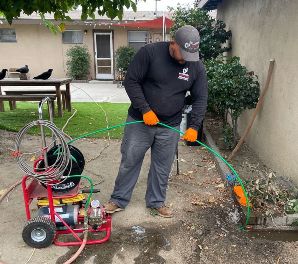 Professional technician using a drain cleaning machine in a residential yard.