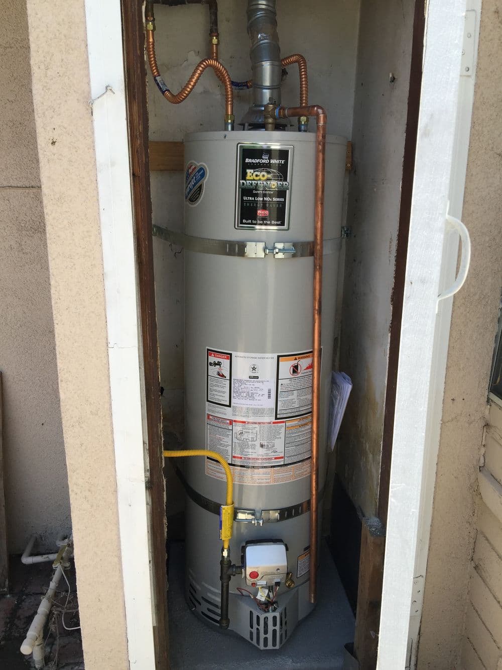 EcoSmart water heater installed in a utility closet with copper piping and safety labels.