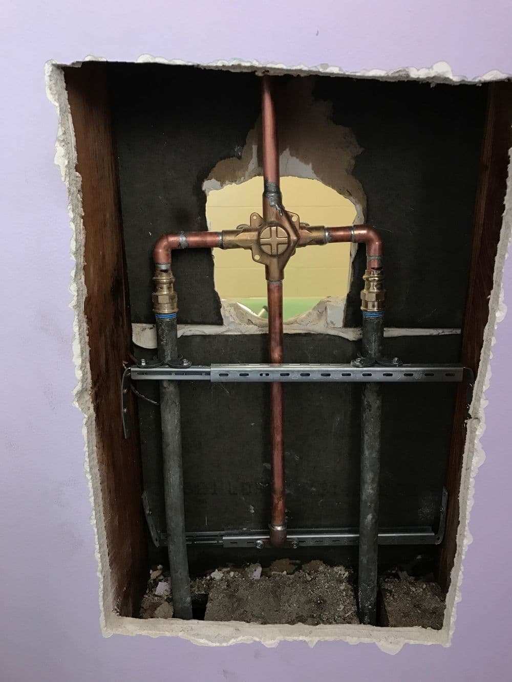 Exposed plumbing with copper pipes and a valve in a wall opening for renovation.