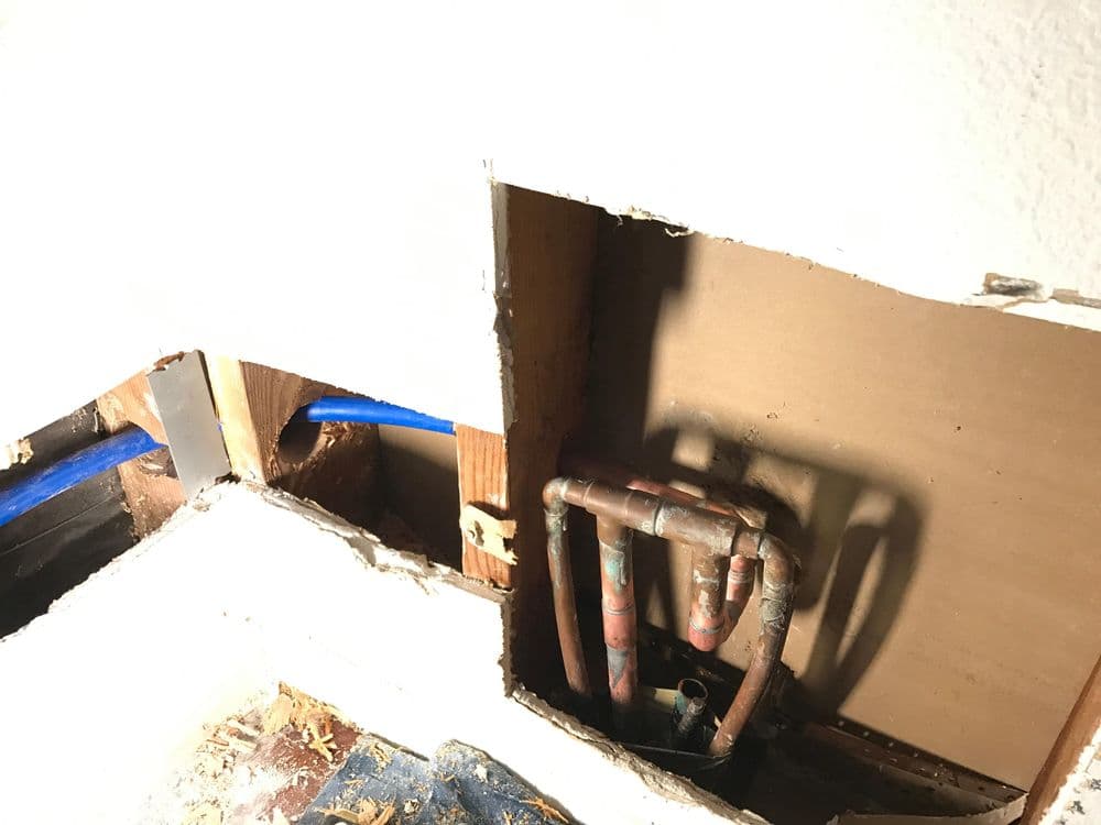 Exposed plumbing behind wall cutout with copper pipes and blue water lines visible.