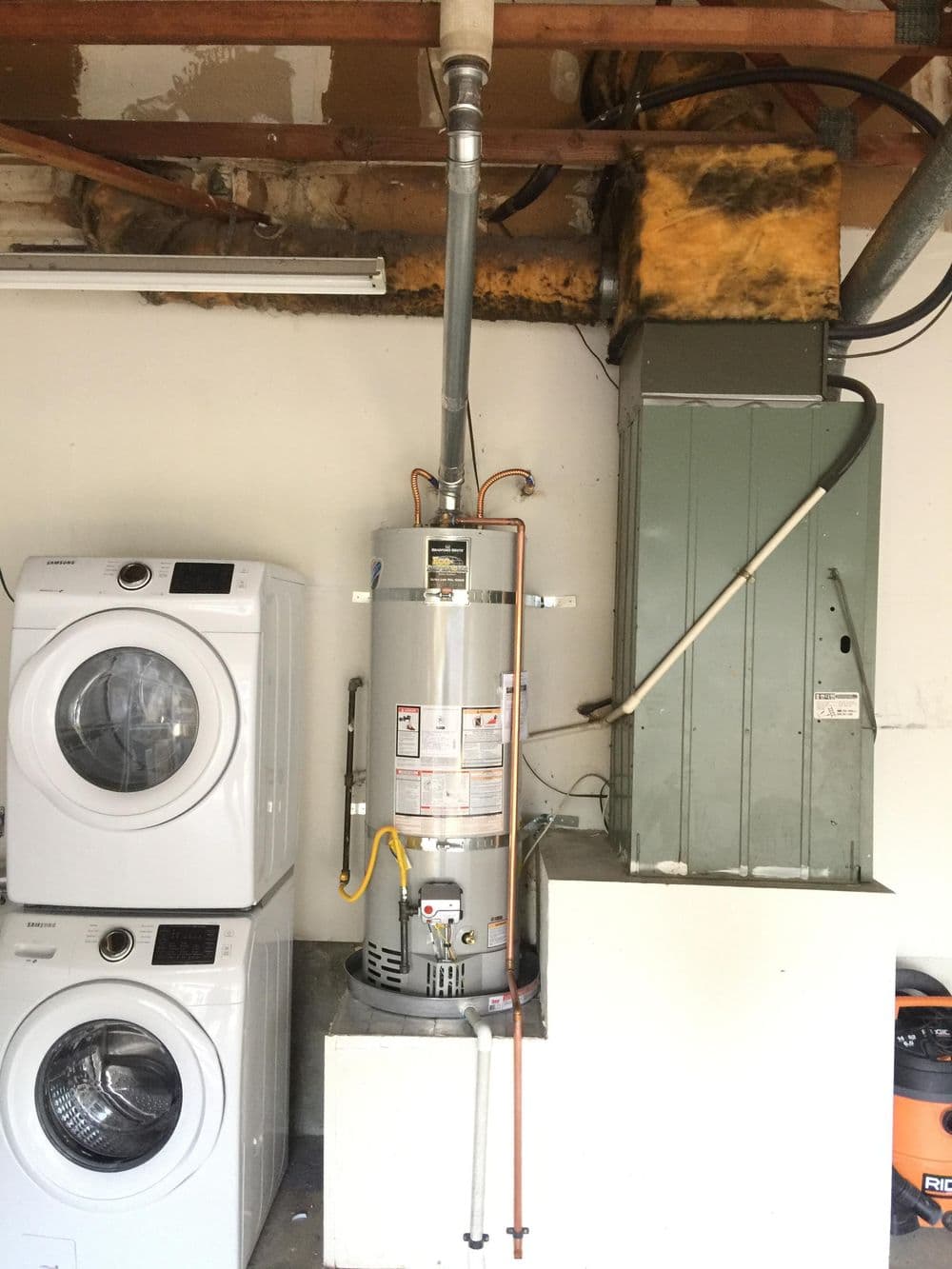 Water heater and HVAC unit in a garage next to washing machines, showcasing home utility setup.