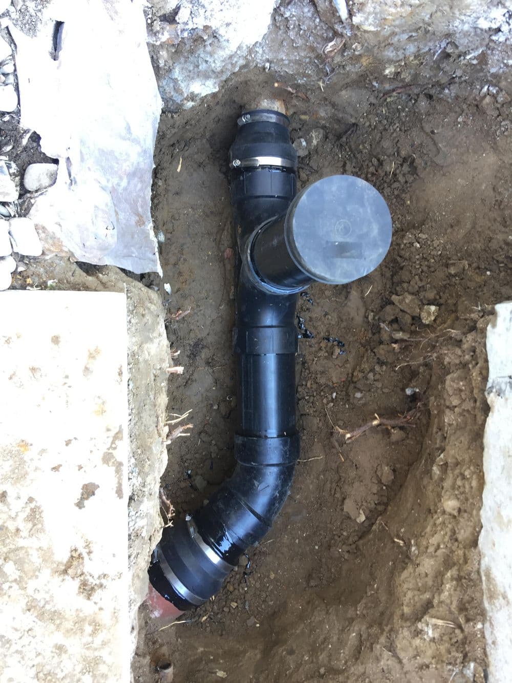 Underground black PVC pipe installation in a trench with surrounding soil.