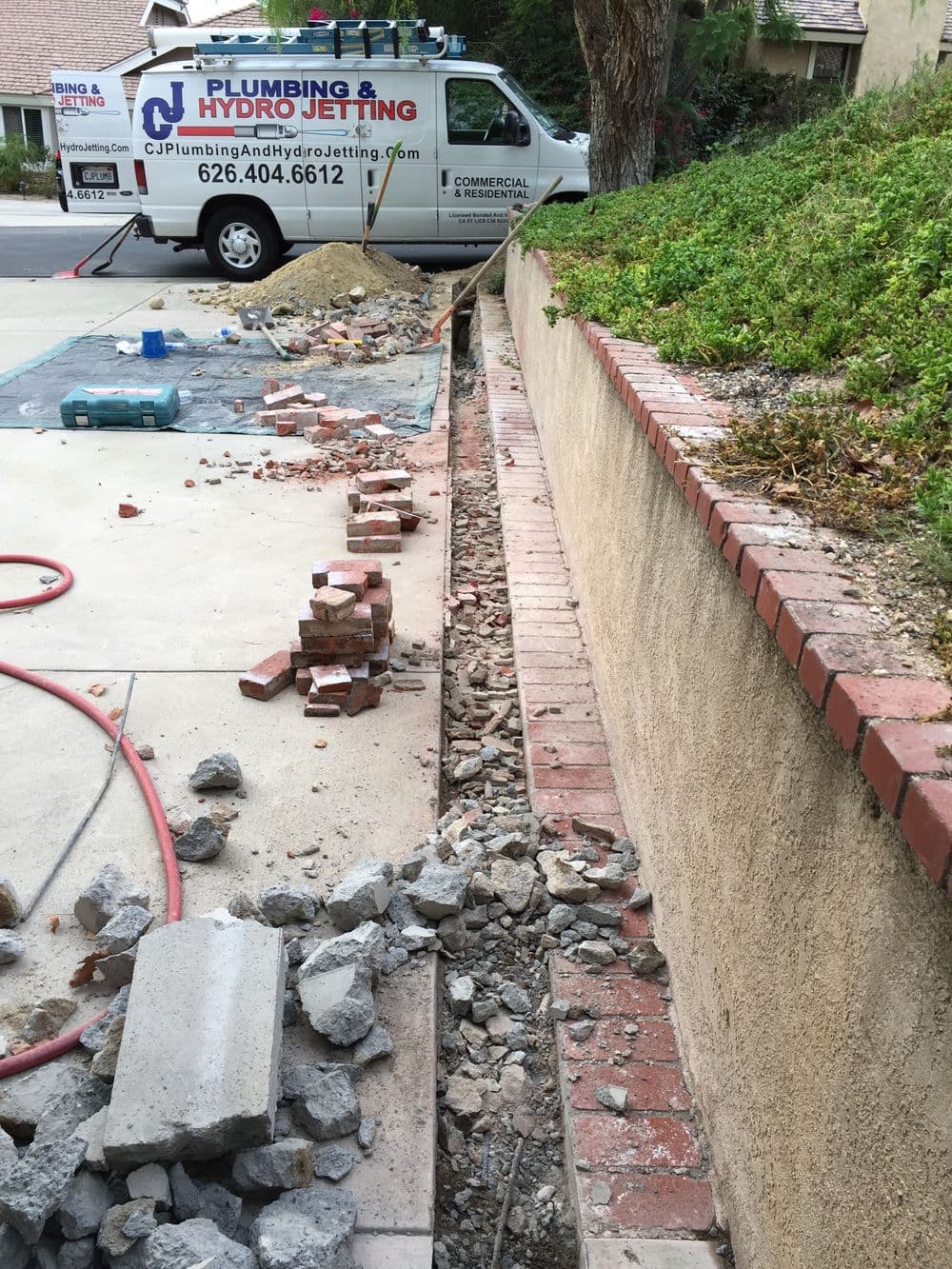 Plumbing service vehicle near a brick-lined trench with construction debris and tools.