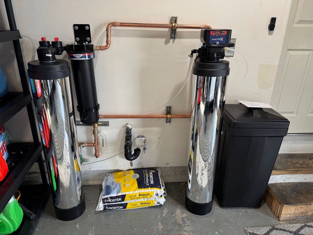 Water filtration system installation with chrome tanks and copper piping in a garage setting.