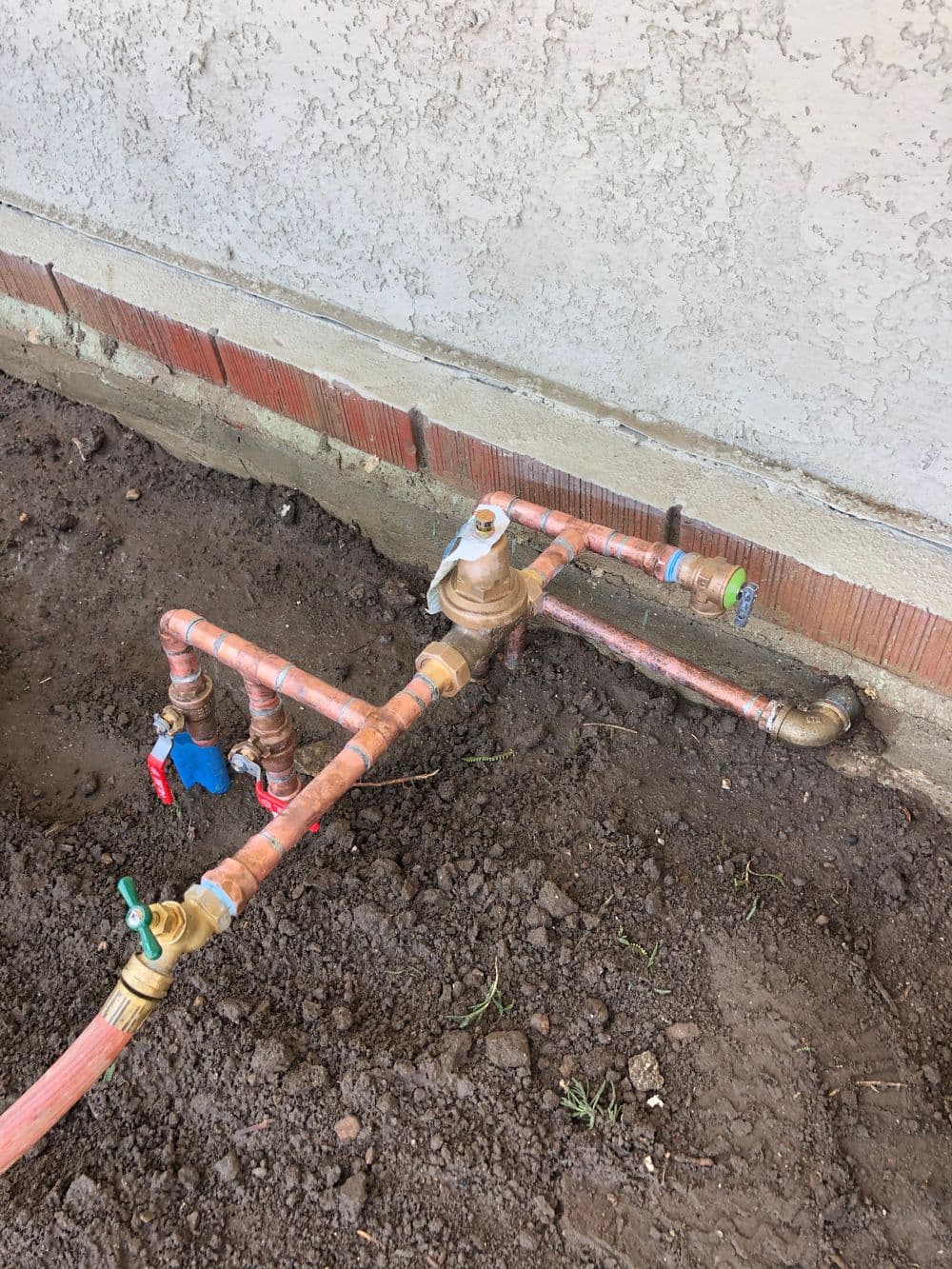 Water meter installation with copper pipes and valves near a building's foundation.