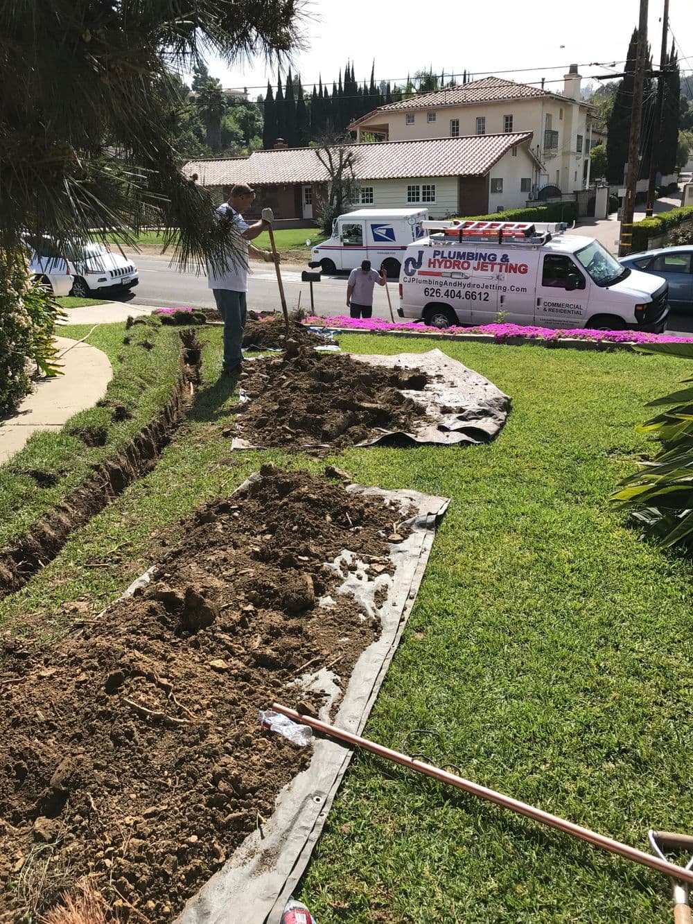 Landscape excavation for plumbing installation, with worker and equipment visible.