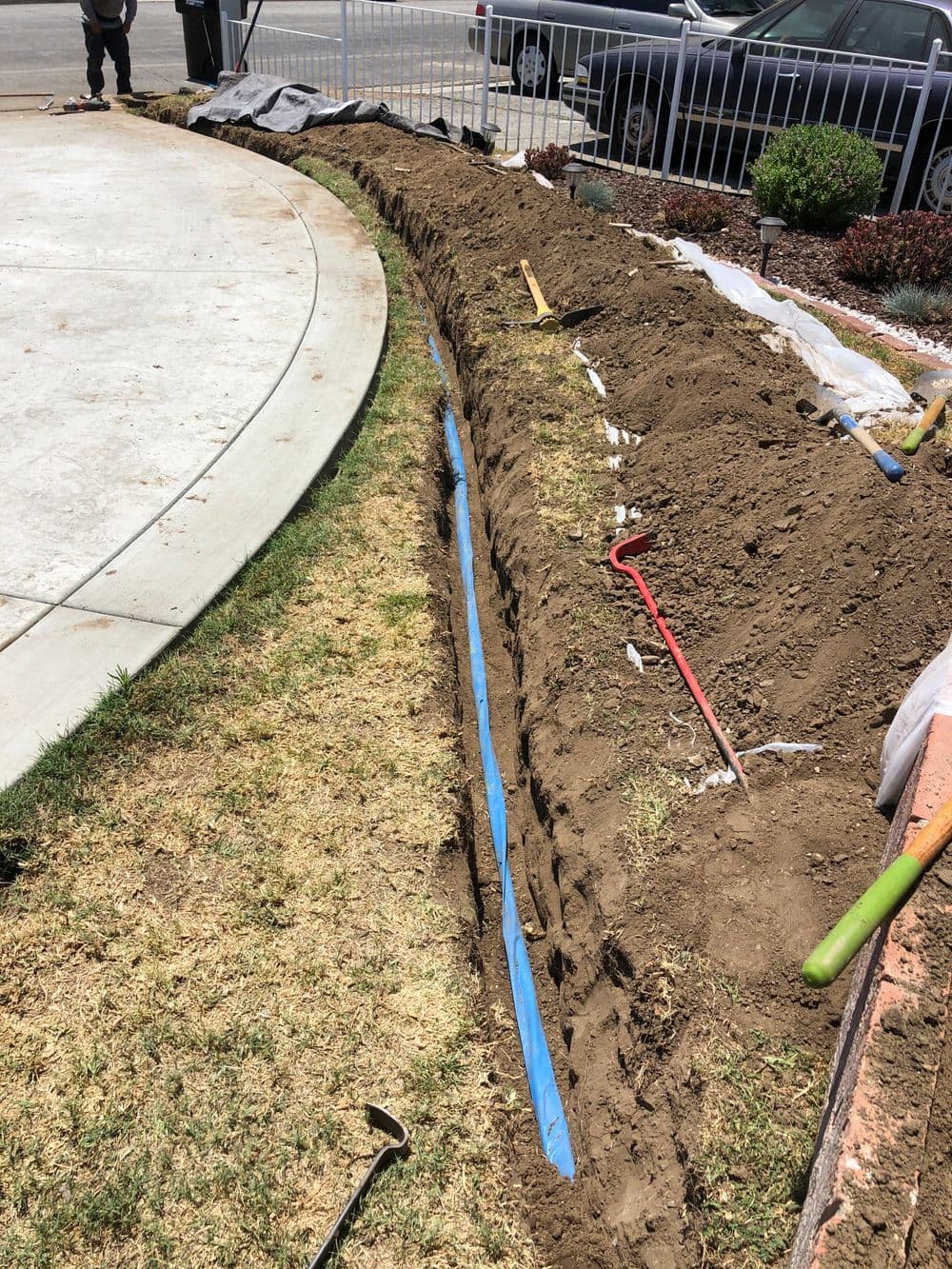 Trench for irrigation installation with tools visible on the ground and grass nearby.