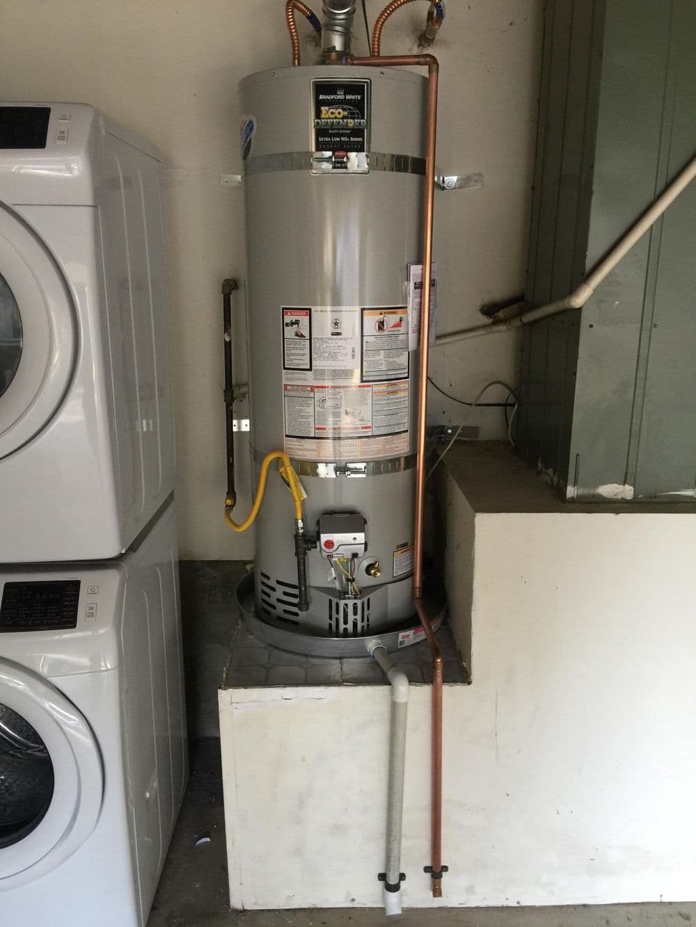 Residential water heater installation with copper and PVC piping in a garage setting.