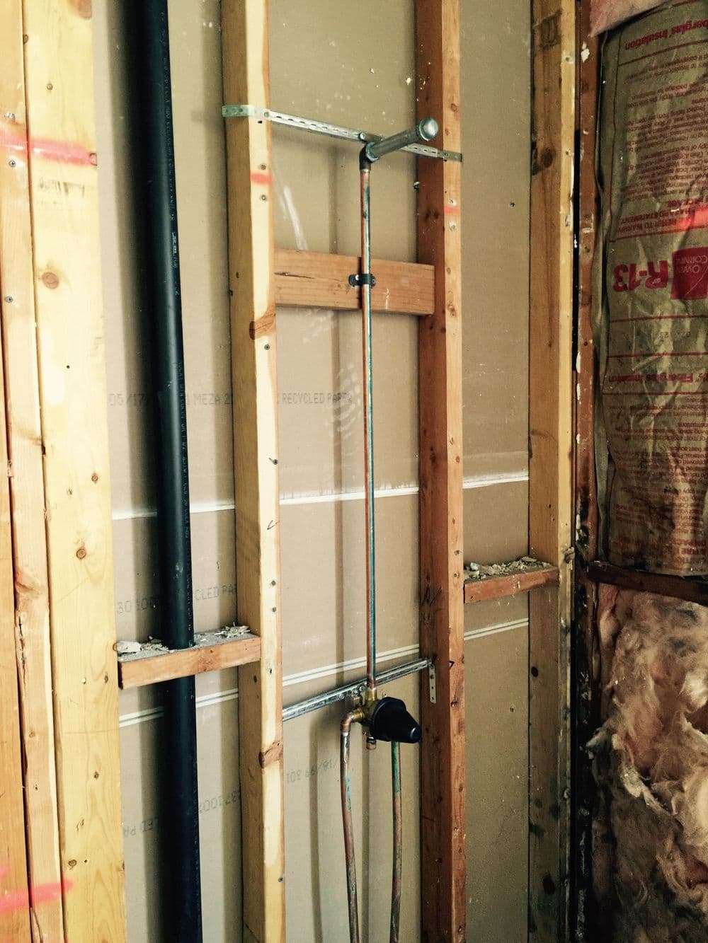 Exposed bathroom plumbing and framing during renovation project with insulation visible.