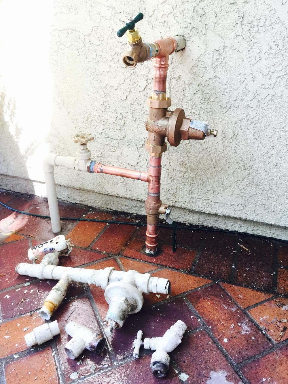 Plumbing system with copper and PVC pipes, including valves and fittings, on a tiled surface.
