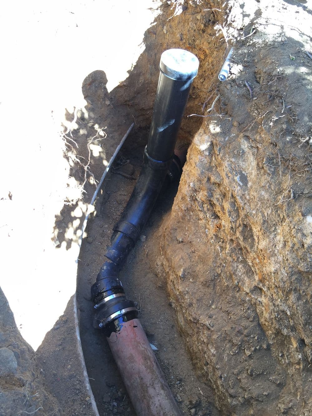 Pipe installation in a trench, showing connection between black and orange drainage pipes.