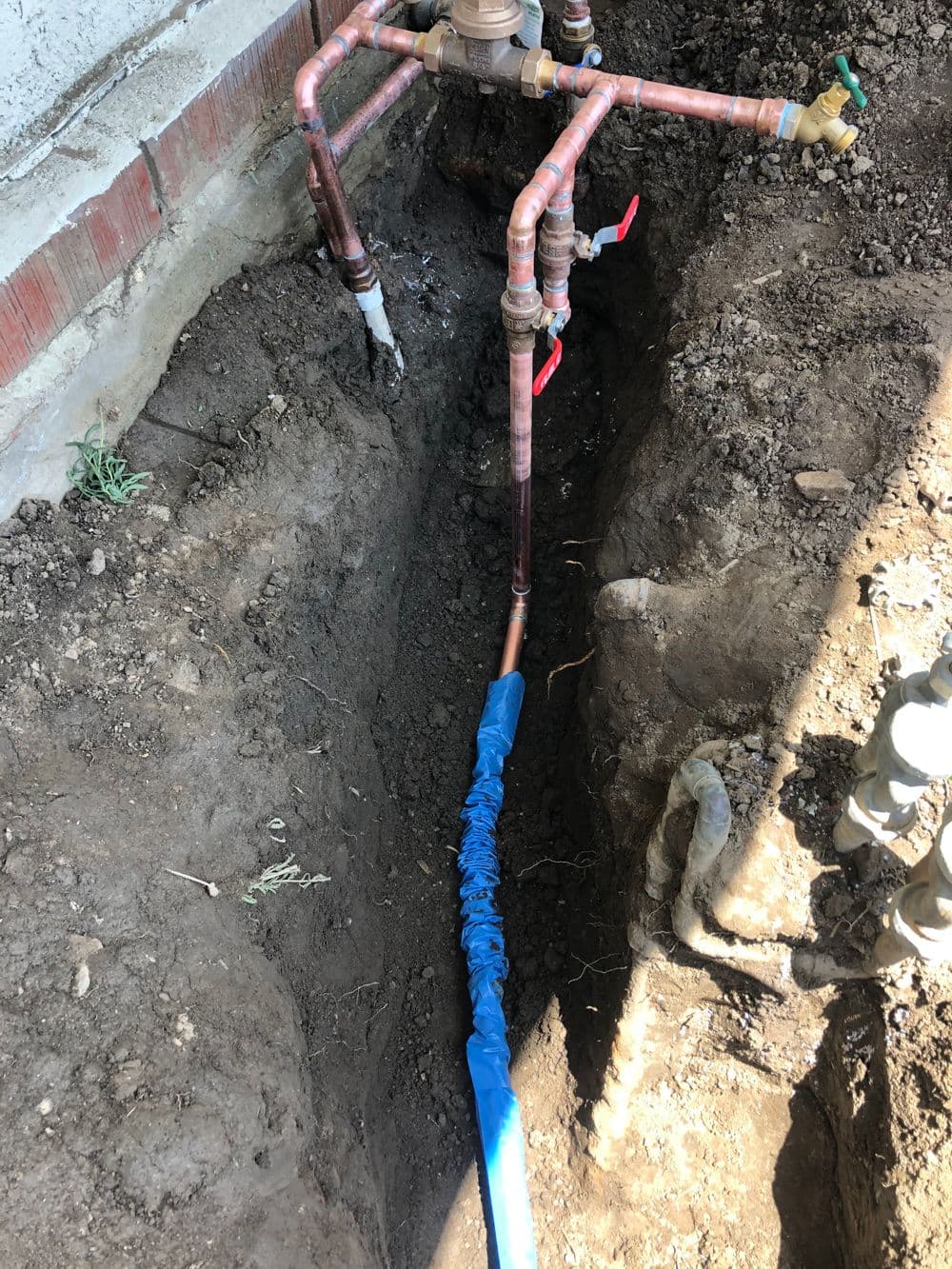 Copper plumbing and a blue insulated pipe installed in a trench for water supply.