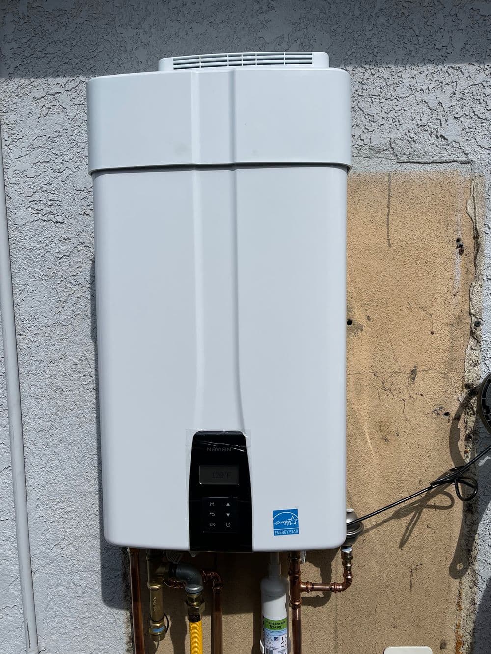 Tankless water heater mounted on a wall, displaying digital temperature control.