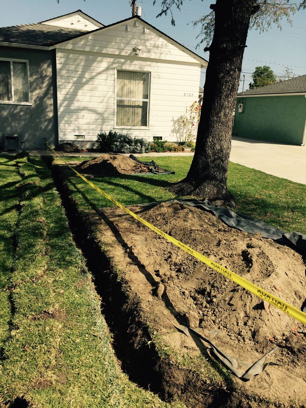 Digging site with exposed soil and tarp beside a house under clear sky, preparing for landscaping.