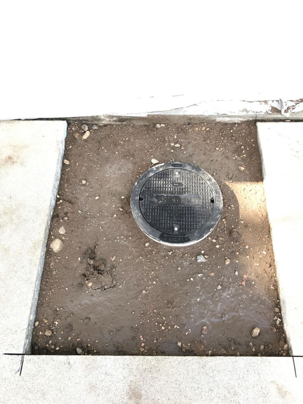Manhole cover surrounded by freshly dug dirt and gravel on a construction site.