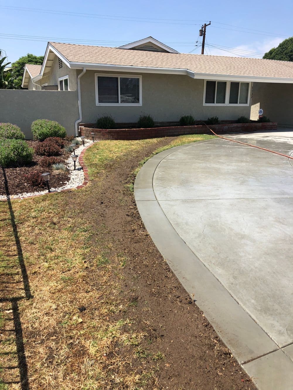 Lawn renovation with freshly edged soil next to a newly poured concrete driveway and home.