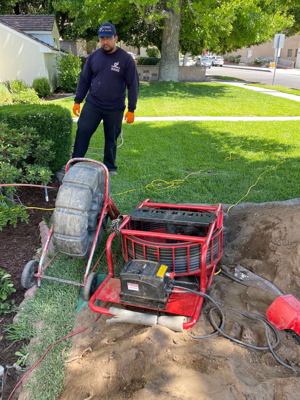 Landscaper operating a red lawn aerator in a residential yard under a sunny sky.