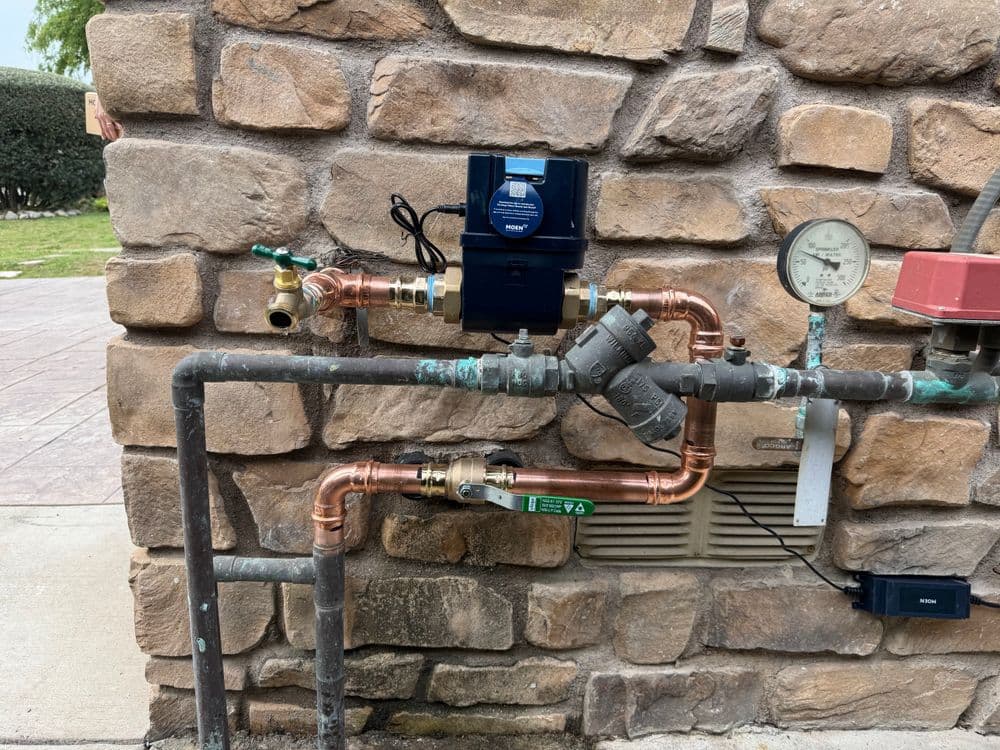 Water meter and plumbing setup against a stone wall, showcasing copper and PVC pipes.