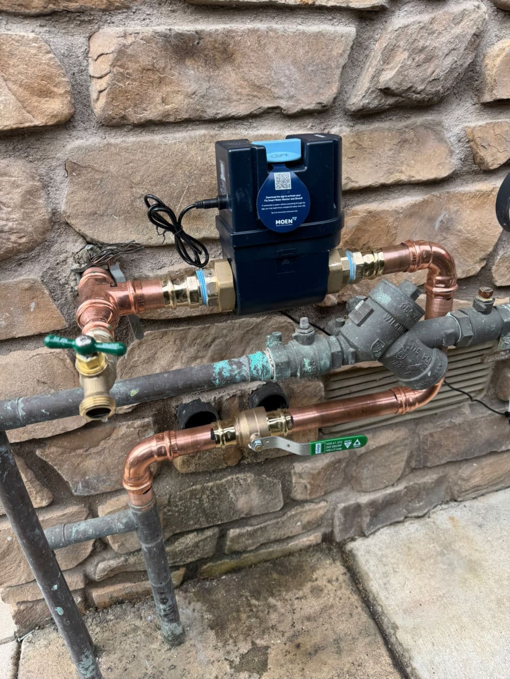 Water pressure regulator with copper and brass fittings mounted on a stone wall.