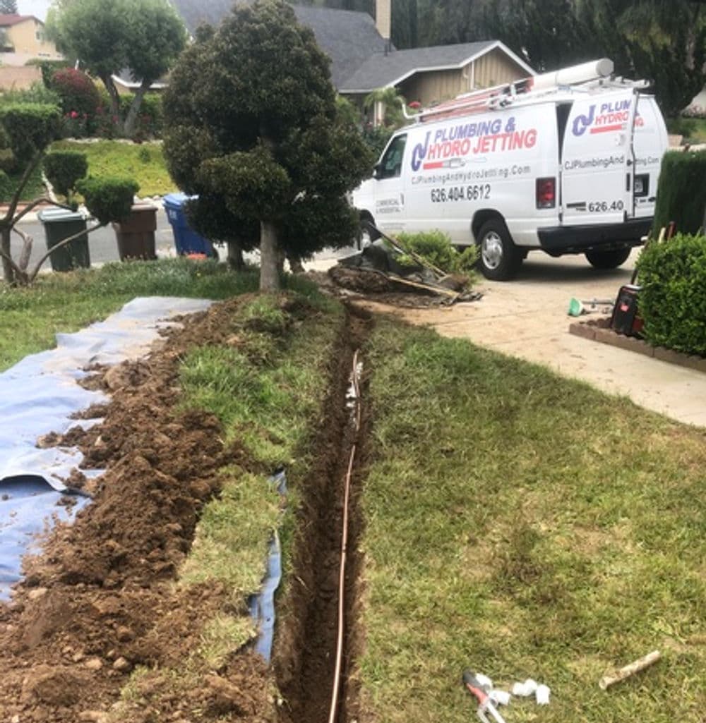 Trenched yard for plumbing installation with hydro-jetting service vehicle in background.