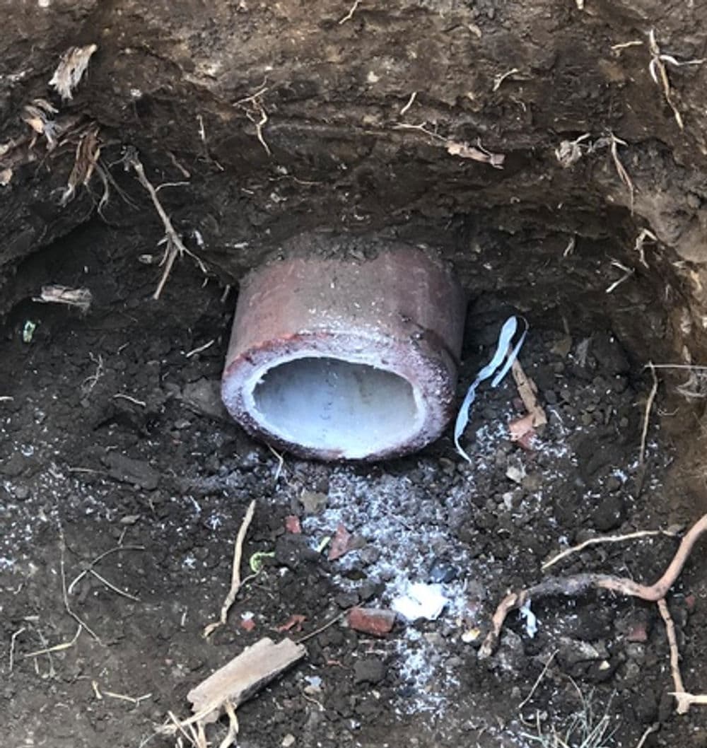 Buried pipe in soil, showing dirt, roots, and debris around it.