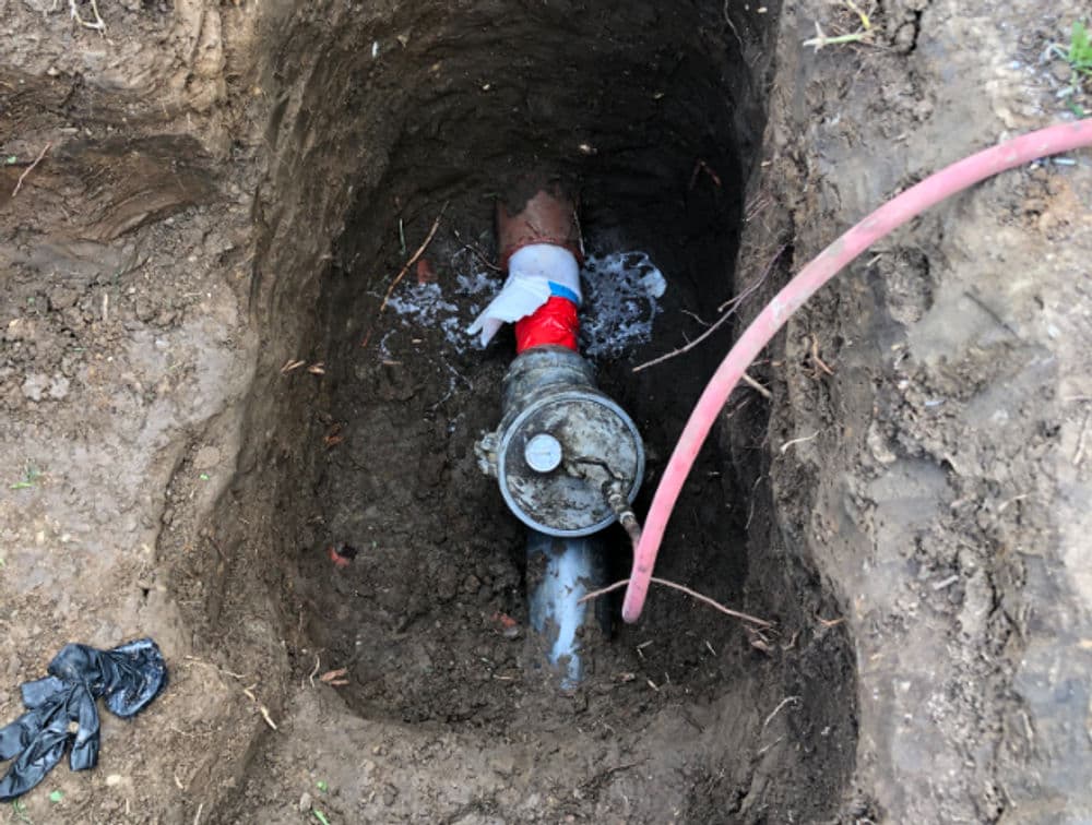 Water pipeline repair in a trench with visible pipe, gloves, and water flow.