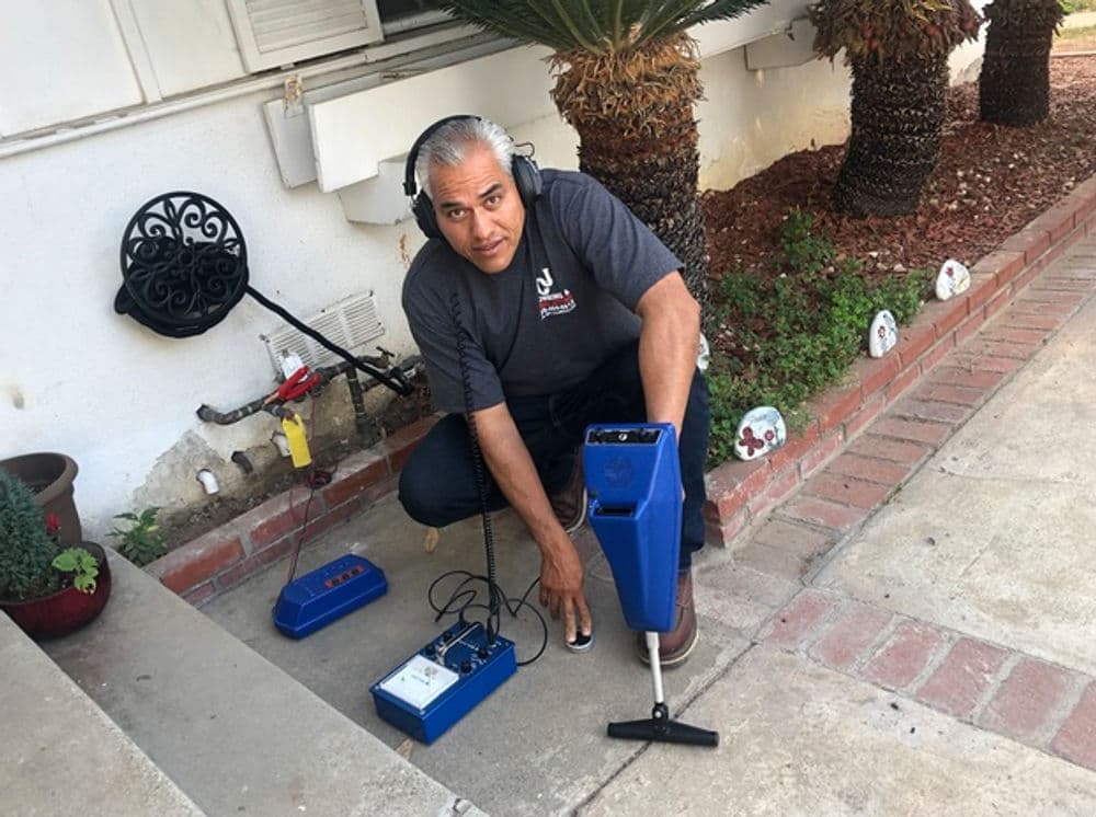 Man using metal detector outdoors, equipped with headphones and a blue detection device.