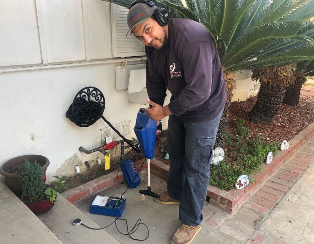 Technician using equipment for pest control outside a home with palm trees in the background.