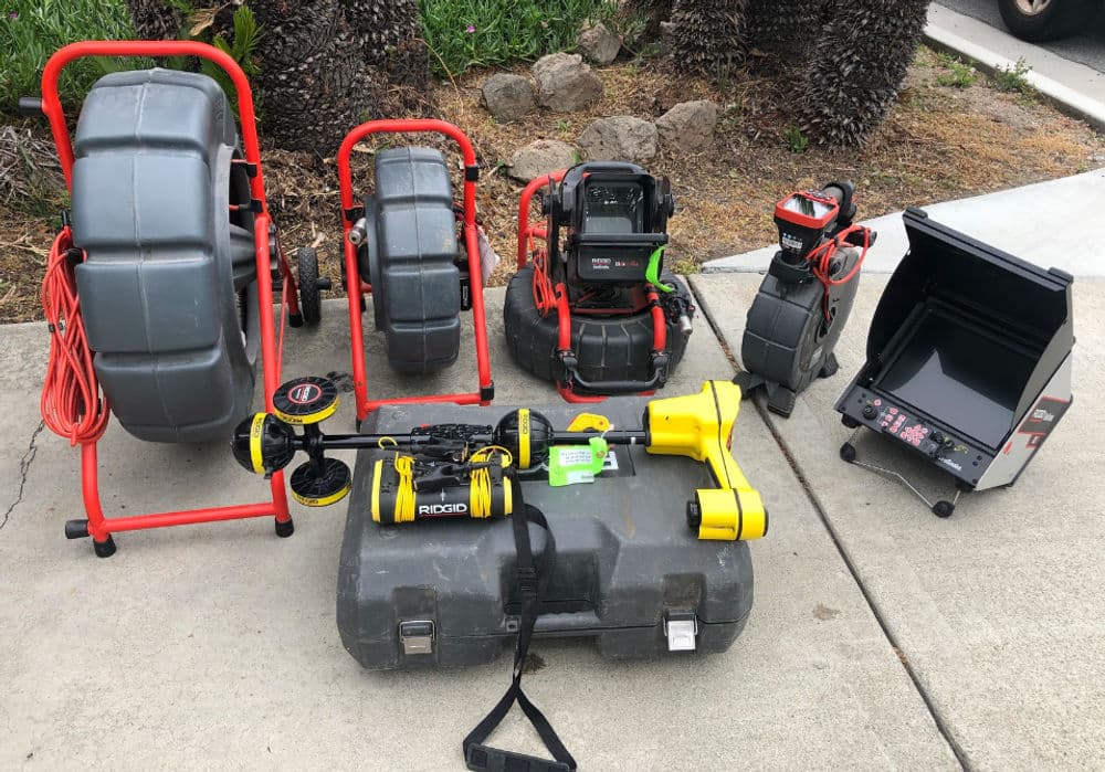 Various plumbing tools and equipment laid out on concrete surface for maintenance tasks.